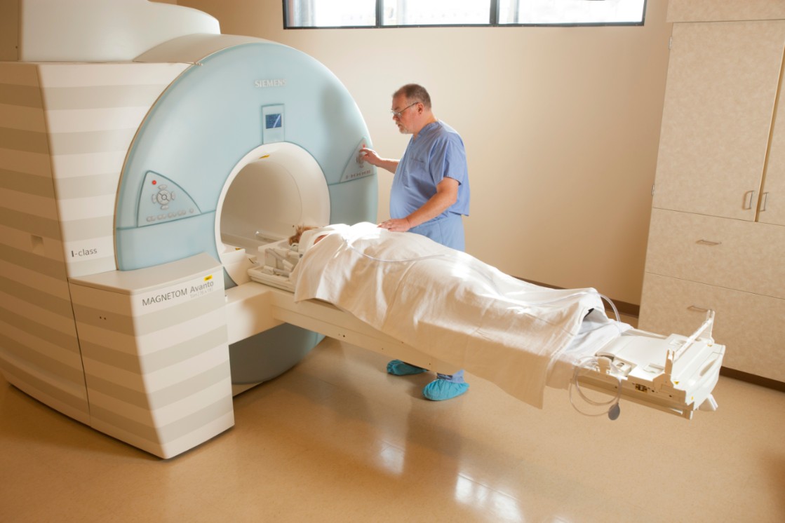 Man operating MRI machine as a patient is prepped for the MRI exam